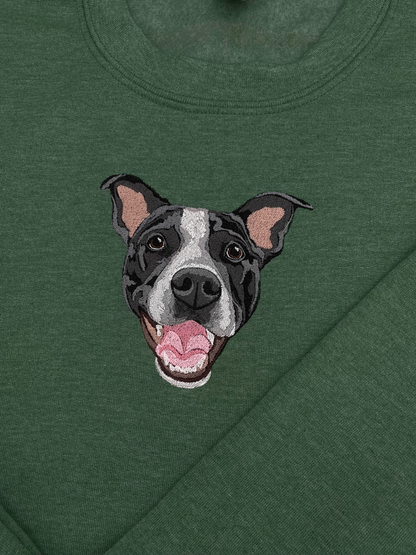 A green crewneck sweatshirt with a embroidered depiction of a custom dog's face in a happy expression.
