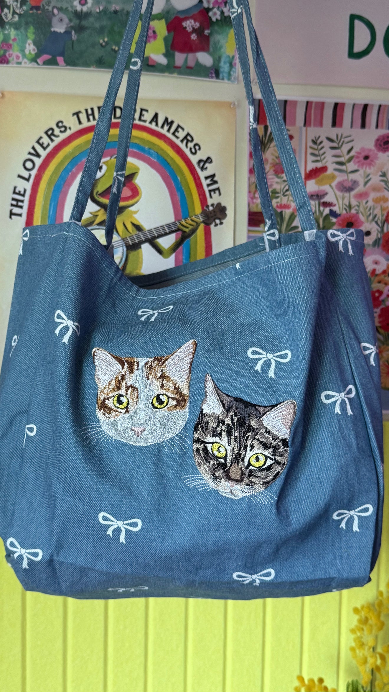 Blue tote bag with cat designs and white bows against a colorful background