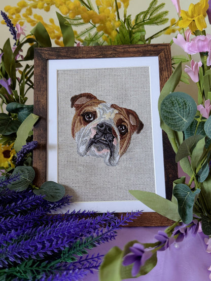 Embroidered picture of a dog's face in a wooden frame surrounded by flowers