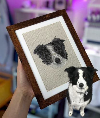 Framed embroidered portrait of a dog held by a person next to a real black and white dog.