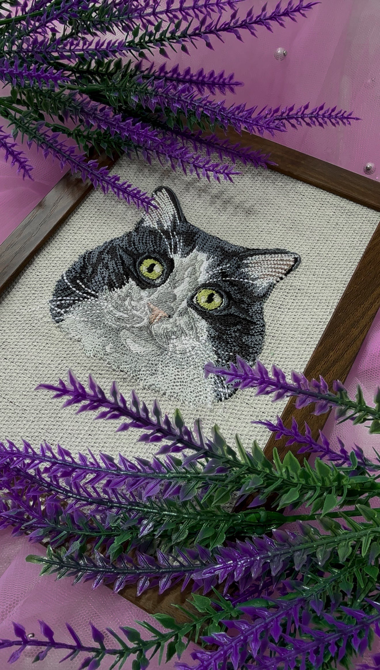 Embroidery of a cat surrounded by purple and green leaves on a pink background