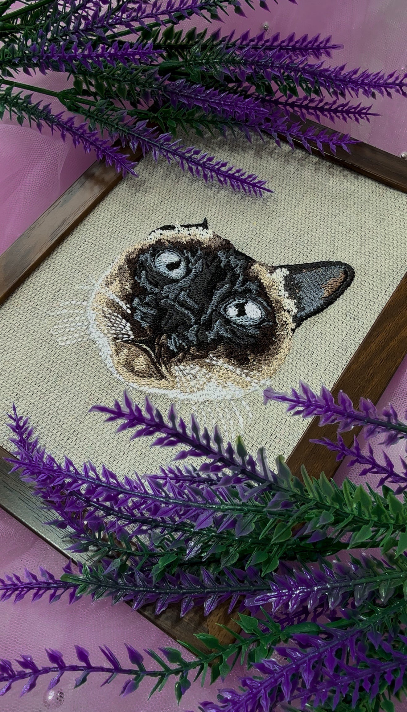 Embroidery of a cat face on fabric with purple and green decorative elements.