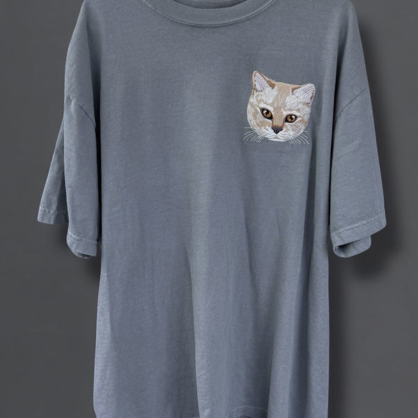 A gray Comfort Colors 100% Cotton T-shirt with a embroidered image of a cat's face on the upper left side.