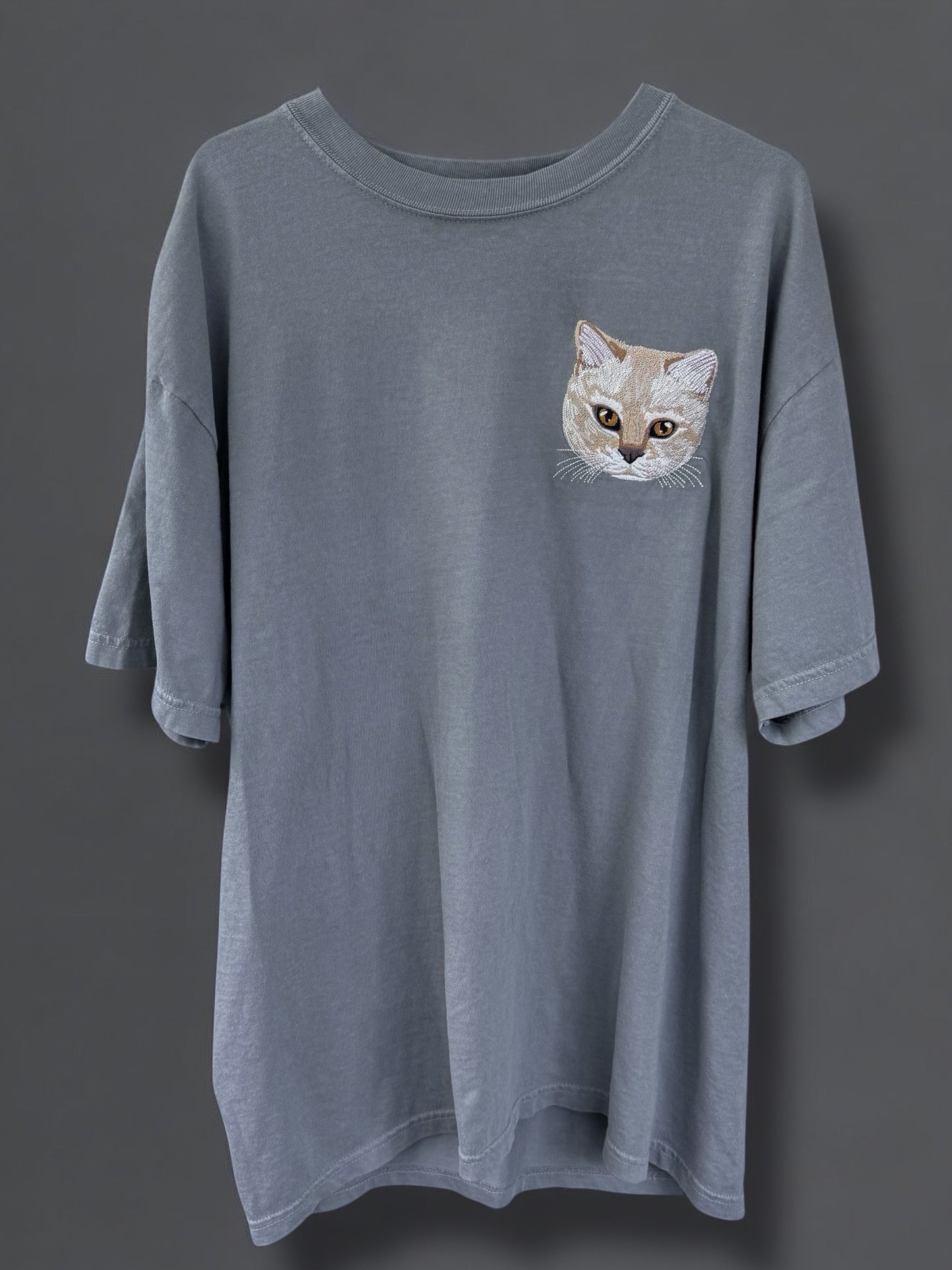 A gray Comfort Colors 100% Cotton T-shirt with a embroidered image of a cat's face on the upper left side.