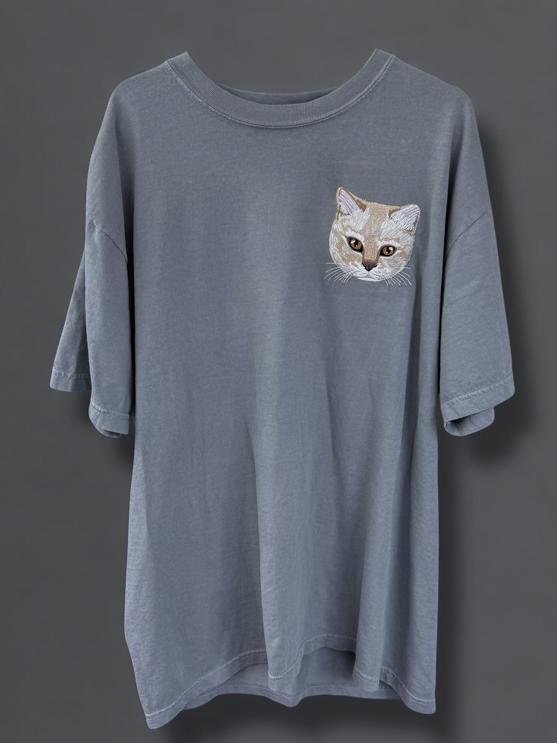A gray Comfort Colors 100% Cotton T-shirt with a embroidered image of a cat's face on the upper left side.