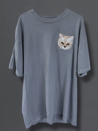A gray Comfort Colors 100% Cotton T-shirt with a embroidered image of a cat's face on the upper left side.