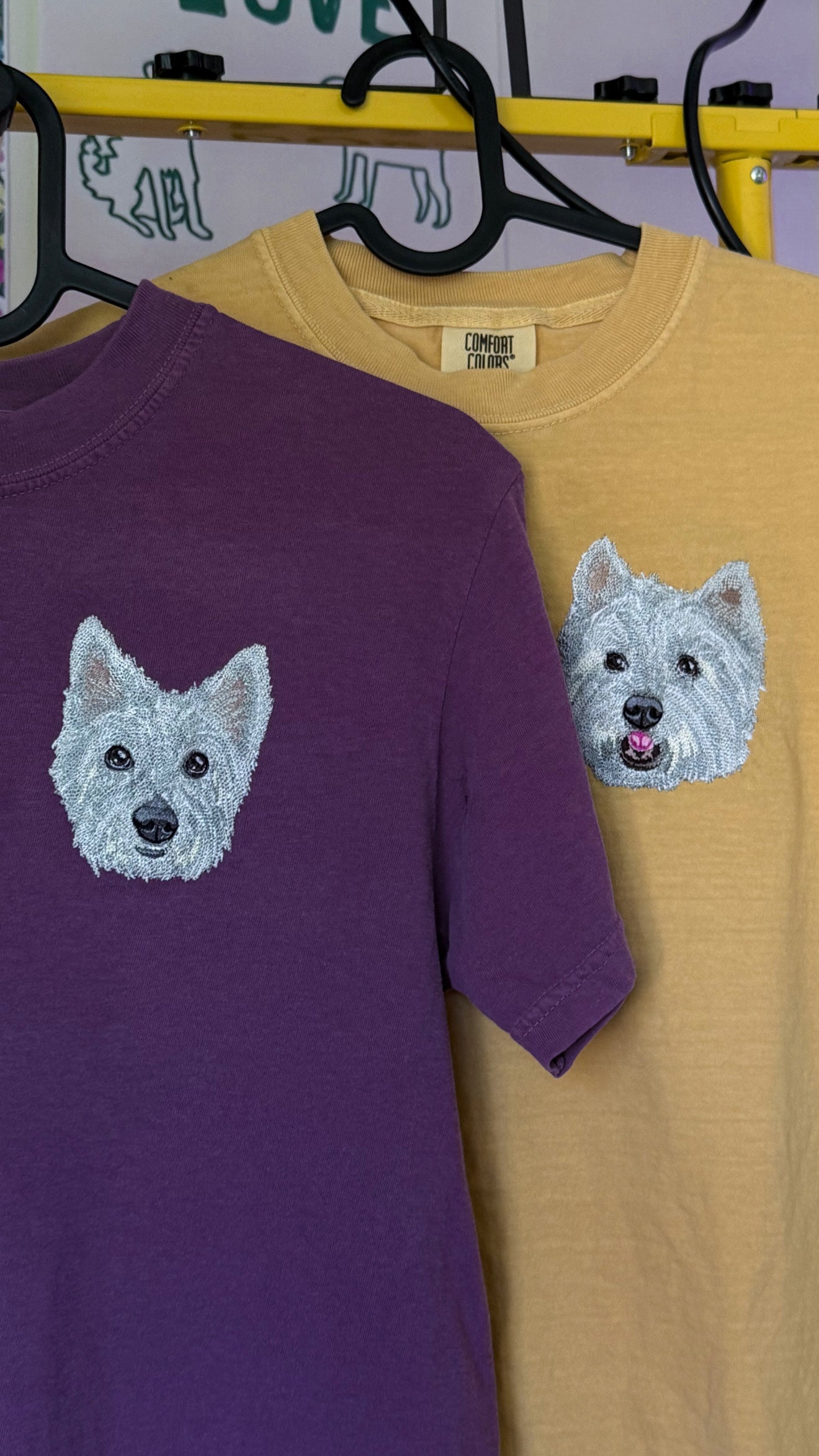 Purple and yellow t-shirts with custom pet embroidered dog faces on a hanger.