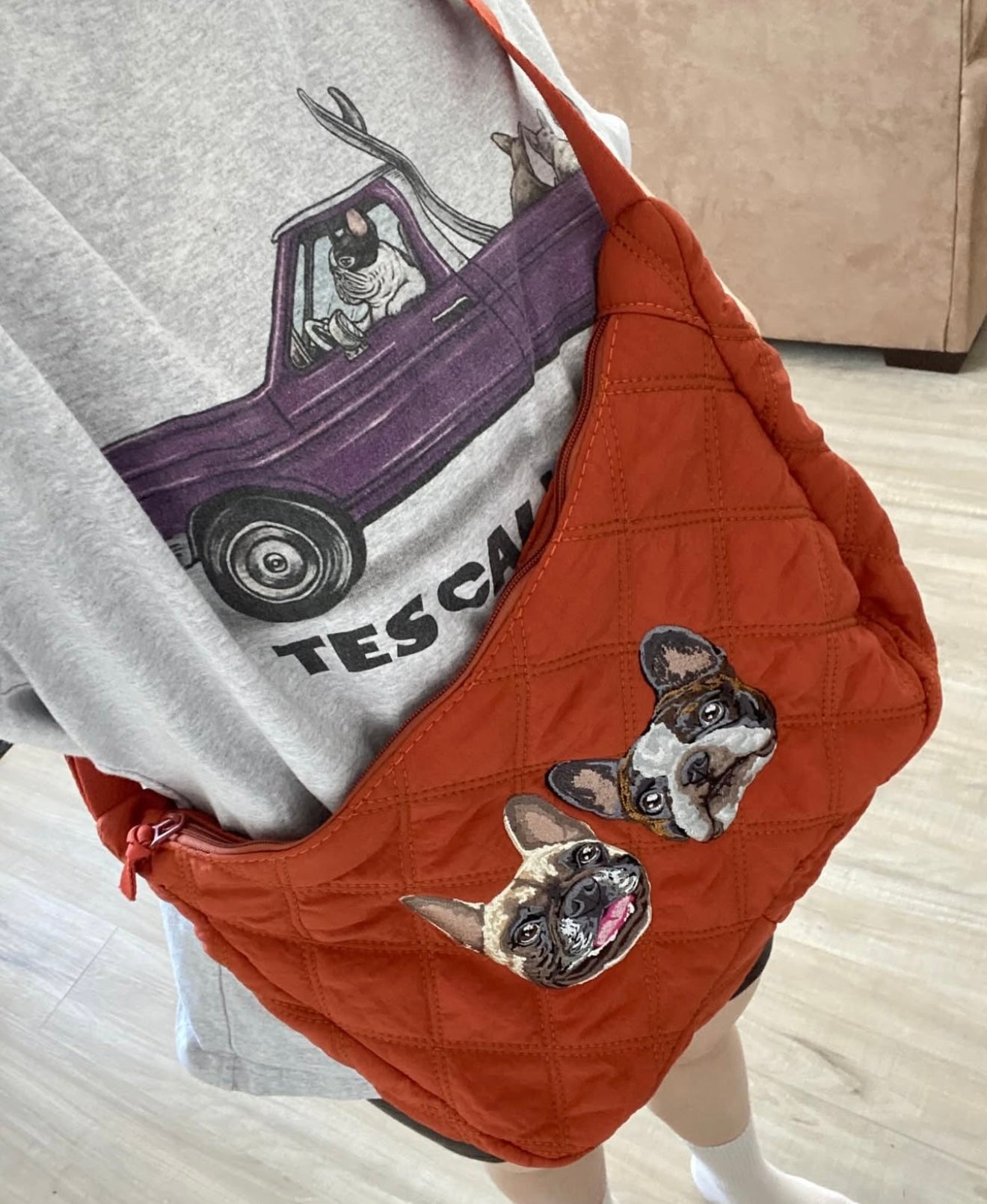 Person wearing a gray sweatshirt with a purple car graphic, paired with an orange bag featuring a dog patch.