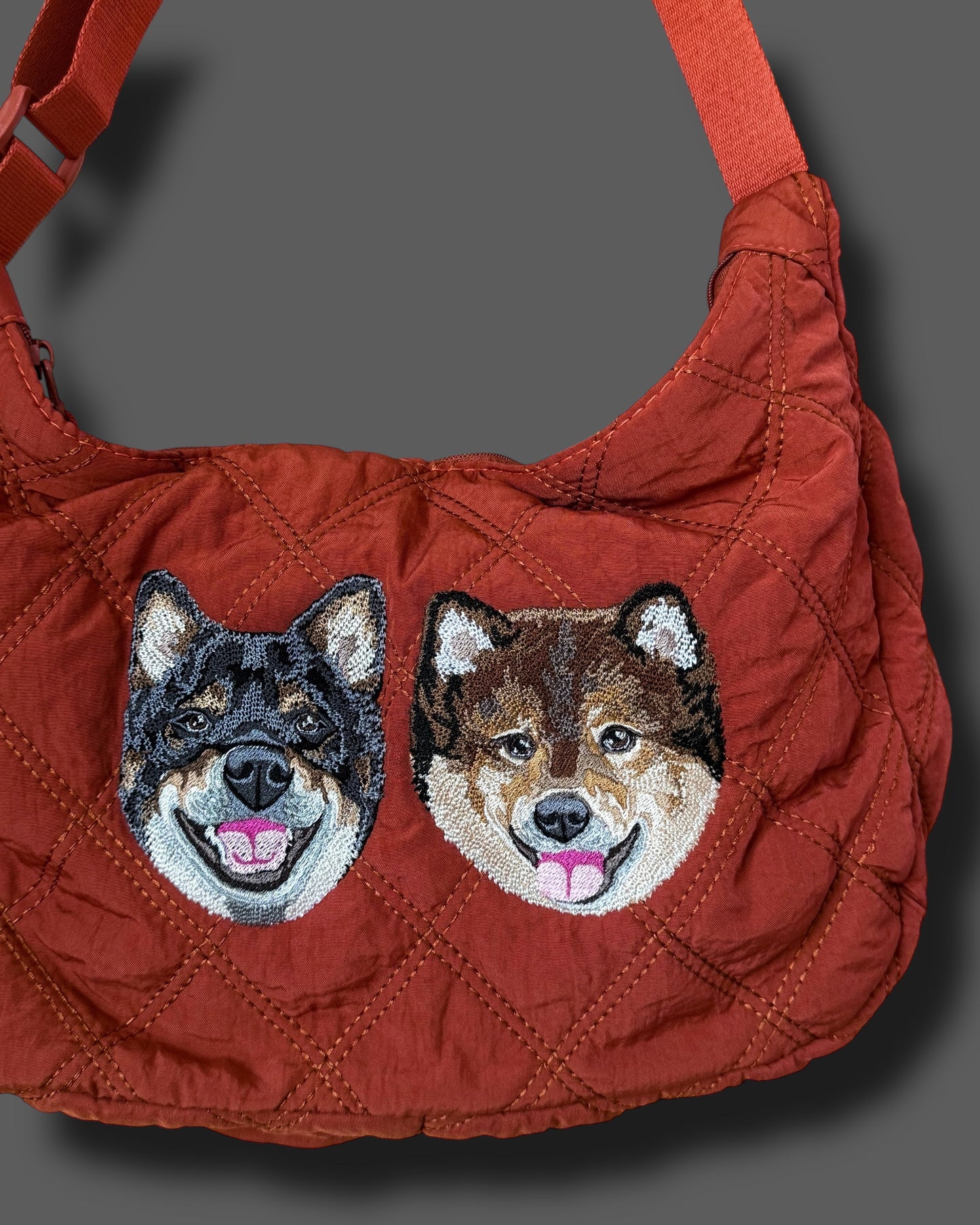 Red quilted handbag with embroidered dog faces on a gray background