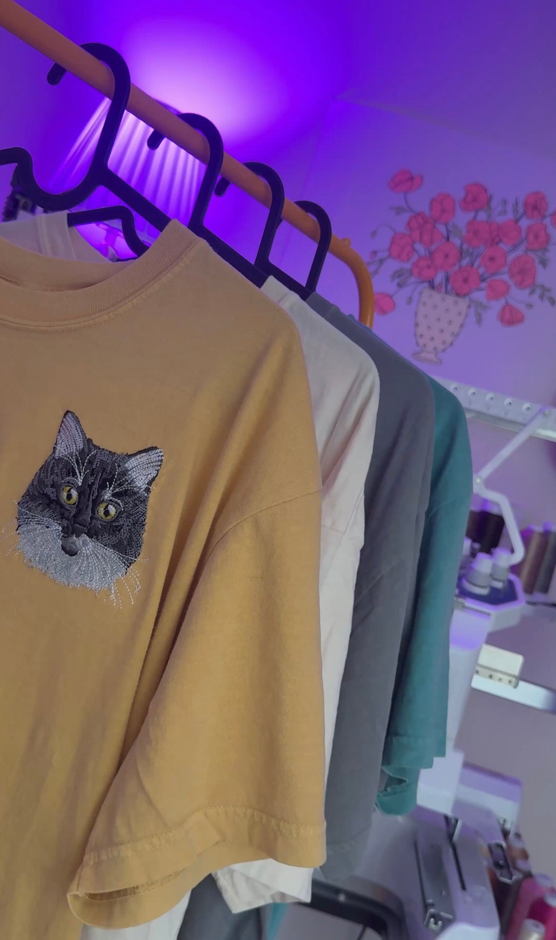 Rack of custom pet embroidered tshirts in a purple lit room